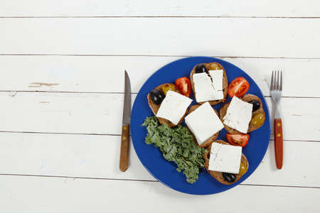 white feta greek cheese sandwich rye bread on blue plate with black spain olives tomatoes and cutlery over retro wooden tableの写真素材