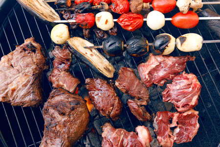 fresh raw beef fillet steak red meat with tomatoes and eggplant on skewers on big round barbecue brazier grid full with ready charcoalの写真素材