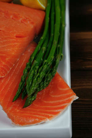 fresh raw salmon fillet served with lemon and white wine in wineglass, wooden barrel, bottle, on white plate over vintage wood table with handmade cutlery knife and forkの写真素材