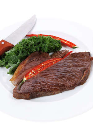 grilled beef steak meat with red hot pepper and fresh raw kale leaf served on white plate isolated over white backgroundの写真素材