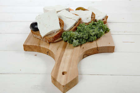 fresh greek feta cheese sandwich on wooden plate with hot green olives and black, goat cube, tomatoes kale over tableの写真素材
