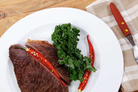 grilled beef steak fillet meat with red hot pepper and  raw kale leaf with ketchup sauce served on white plate over wood tableの写真素材
