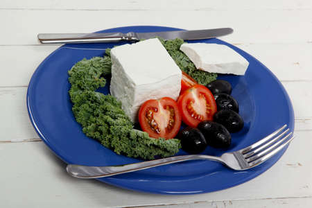 white goat feta cheese with black olives and tomatoes on blue plate over wooden tableの写真素材