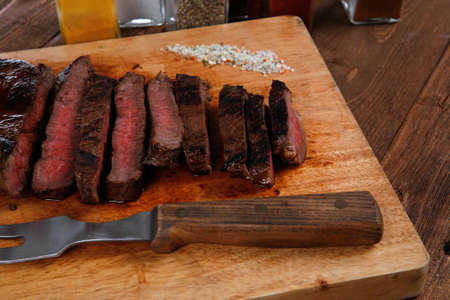 fresh roast red beef meat fillet mignon cutted on wooden plate with vintage fork many different kinds of dry spice over tableの写真素材