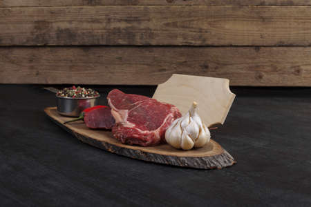 fresh raw beef piece fillet on middle size wooden plate with pepper and peppercorns in measuring spoon with name plate space for text on black backgroundの写真素材
