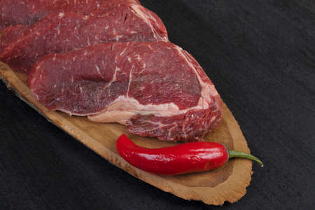 fresh raw beef piece fillet on middle size wooden plate with pepper and peppercorns in measuring...