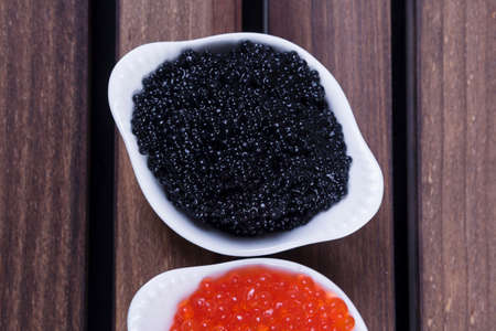 black sturgeon hausen caviar with red salmon caviar in white bowls on wooden backgroundの写真素材