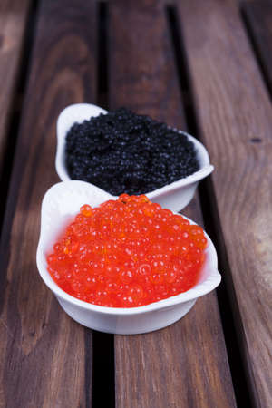 black sturgeon hausen caviar with red salmon caviar in white bowls on wooden backgroundの写真素材