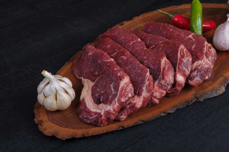 fresh raw beef pieces fillet on big size wooden plate with pepper and peppercorns in measuring spoon space for text on black backgroundの写真素材