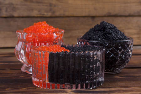 fresh raw red salmon caviar with black sturgeon caviar in white crystal bowls on burned vintage wooden table backgroundの写真素材