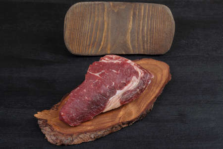 fresh raw beef piece fillet on small wooden plate with pepper peppercorns and nameplate space for text on black backgroundの写真素材