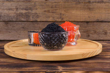 fresh raw red salmon caviar with black sturgeon caviar in white crystal bowls on burned vintage wooden table backgroundの写真素材