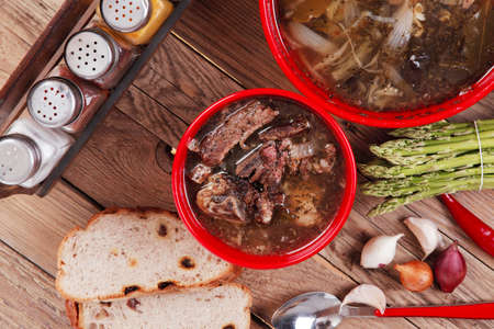 home style beef meat soup vintage country wood table asparagus pepper bell spices bread garlic cutlery spices red bowlsの写真素材
