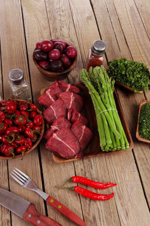 fresh beef meat asparagus greenery spices cutlery wooden table pepper crushed hot chili vegetables bowl servedの写真素材