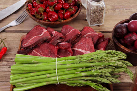 fresh beef meat asparagus greenery spices cutlery wooden table pepper crushed hot chili vegetables bowl servedの写真素材