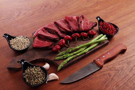 fresh beef meat asparagus greenery spices cutlery wooden table pepper crushed hot chili vegetables bowl served garlic cutting boardの写真素材