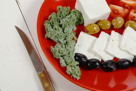 fresh greek feta cheese sandwich on red plate with hot green olives and black, goat cheese cube, tomatoes kale over retro tableの写真素材