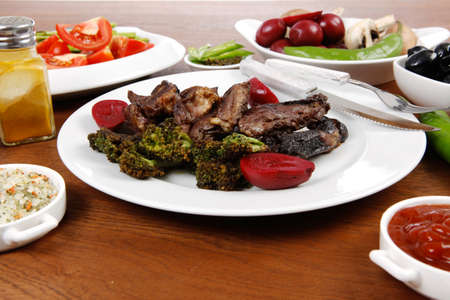 lunch of grilled meat served on big white plate with asparagus pickles tomatoes olives hot black red green pepper salt baked beans and ketchup on wooden tableの写真素材