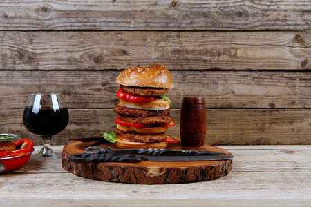 fresh grilled beef huge hamburger served on wood plate with red wine glass chili pepper rosemary green salad leaf and forged vintage antique cutlery over wooden table empty space for textの写真素材