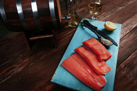 fresh raw salmon fillet served with lemon and white wine in wineglass bottle wooden barrel on blue plate over vintage wood table with forged handmade cutlery knife and 
spice on spoonの写真素材