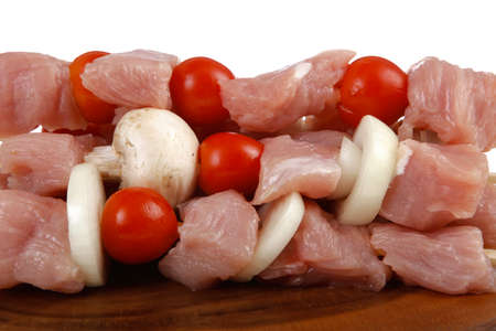 fresh raw meat fillet shish kebab turkey pork pink on skewers tomatoes mushrooms on wooden kitchen plate isolated over white backgroundの写真素材