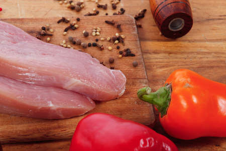 fresh raw turkey meat steak with hot sweet pepper dry spices castor and pepperbox on wood cutting boar over tableの写真素材