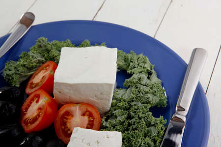 white goat feta cheese with black olives and tomatoes on blue plate over wooden tableの写真素材