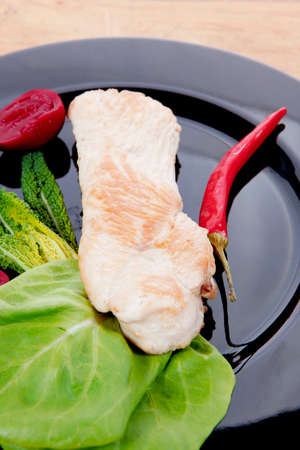 fresh roast turkey meat steak fillet with red hot pepper and green lettuce salad kale on black plate over wooden table with knife and forkの写真素材