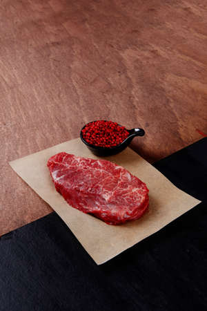 fresh raw beef rib eye steak on black walnut wooden table with red hot pepper spice in saucerの写真素材