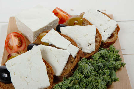 fresh greek feta cheese sandwich on wooden plate with hot green olives and black, goat cube, tomatoes kale over tableの写真素材
