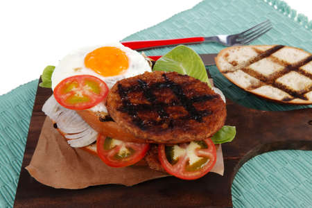 junk food big beef hamburger on dark wood plate with modern cutlery on blue mat isolated over white backgroundの写真素材