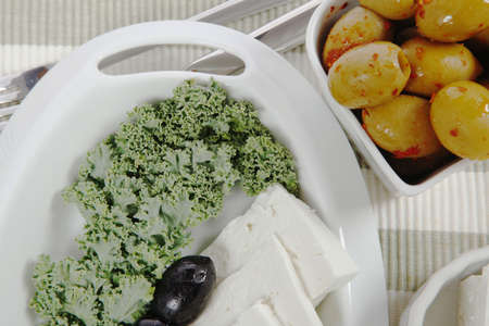 fresh greek feta cheese sandwich on white plate with hot green olives and black, goat cheese cube, tomatoes kale over retro tableの写真素材