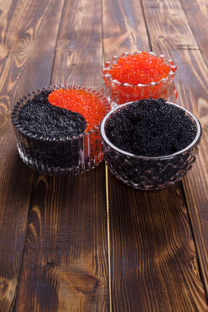 fresh raw red salmon caviar with black sturgeon caviar in white crystal bowls on burned vintage wooden table backgroundの写真素材