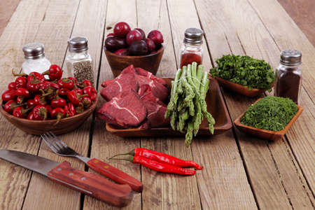 fresh beef meat asparagus greenery spices cutlery wooden table pepper crushed hot chili vegetables bowl servedの写真素材
