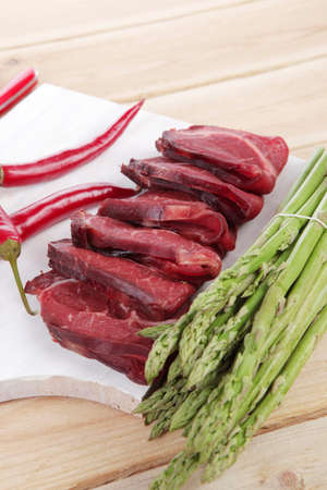 fresh beef meat slices asparagus spices cutlery wooden table pepper hot chili vegetables served garlic light cutting board ready to cookの写真素材