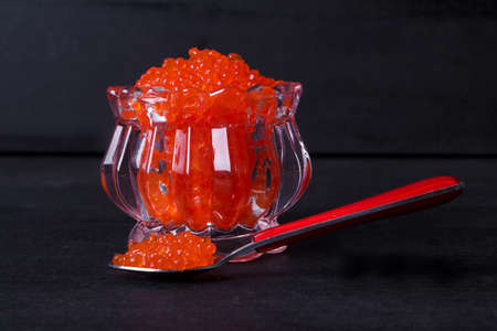 fresh raw red salmon caviar in white crystal bowls with small spoon on blackwooden backgroundの写真素材