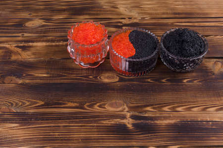 fresh raw red salmon caviar with black sturgeon caviar in white crystal bowls on burned vintage wooden table backgroundの写真素材