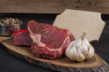 fresh raw beef piece fillet on middle size wooden plate with pepper and peppercorns in measuring spoon with name plate space for text on black backgroundの写真素材