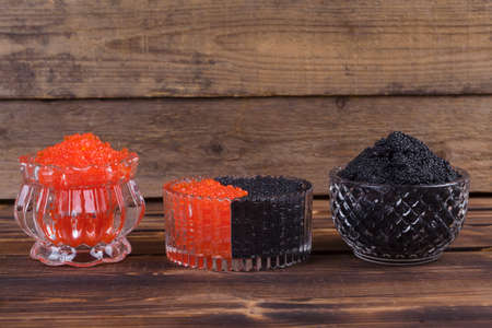 fresh raw red salmon caviar with black sturgeon caviar in white crystal bowls on burned vintage wooden table backgroundの写真素材