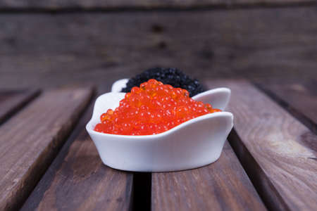 black sturgeon hausen caviar with red salmon caviar in white bowls on wooden backgroundの写真素材