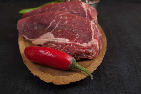 fresh raw beef piece fillet on middle size wooden plate with pepper and peppercorns in measuring spoon space for text on black backgroundの写真素材