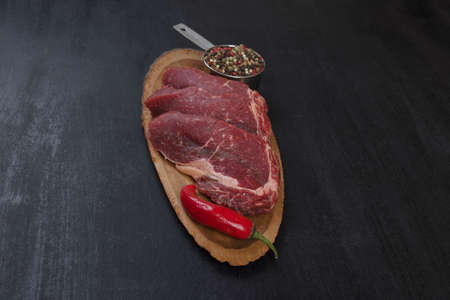 fresh raw beef piece fillet on middle size wooden plate with pepper and peppercorns in measuring spoon space for text on black backgroundの写真素材