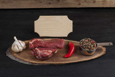 fresh raw beef piece fillet on middle size wooden plate with pepper and peppercorns in measuring spoon with name plate space for text on black backgroundの写真素材