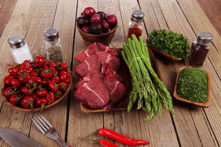 fresh beef meat asparagus greenery spices cutlery wooden table pepper crushed hot chili vegetables bowl servedの写真素材