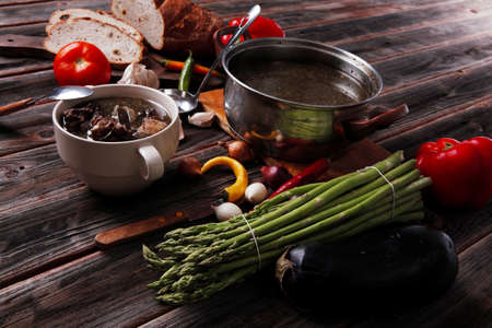 home style beef meat soup vintage country wood table asparagus pepper bell spices bread garlic cutlery eggplantの写真素材