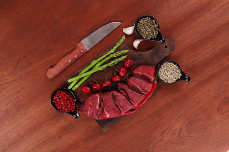 fresh beef meat asparagus greenery spices cutlery wooden table pepper crushed hot chili vegetables bowl served garlic cutting boardの写真素材