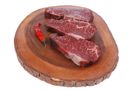 three fresh raw marble beef meat sirloin porterhouse steak on big wooden cutting plate with hot chili pepper isolated on white backgroundの写真素材