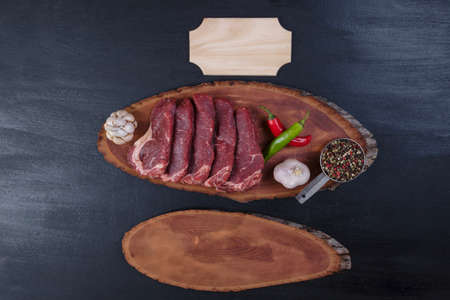 fresh raw beef pieces fillet on big size wooden plate with pepper and peppercorns in measuring spoon name plate space for text on black backgroundの写真素材
