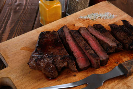 fresh roast red beef meat fillet mignon cutted on wooden plate with vintage fork many different kinds of dry spice over tableの写真素材
