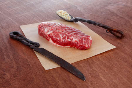 fresh raw beef rib eye steak on walnut table with salt spice and black iron antique forged cutlery fork knifeの写真素材